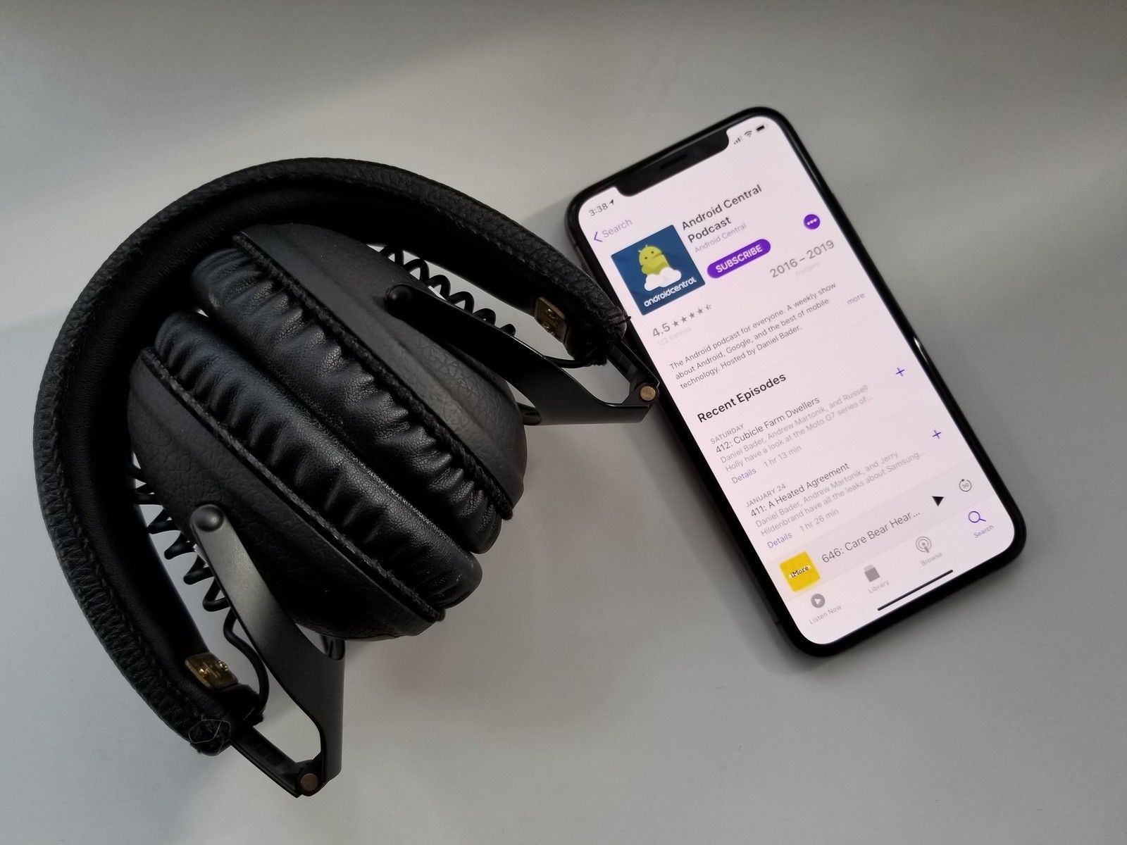 iPhone XS с Apple Podcasts, показывающих страницу подкаста Android Central на белом столе рядом с черными наушниками